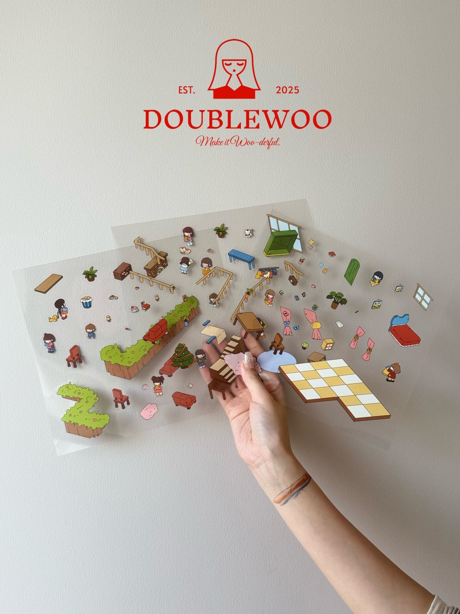 Clear PET sticker sheets showing vibrant characters, party props, green hedges, and casual living room furniture, held by hand for scale and clarity.