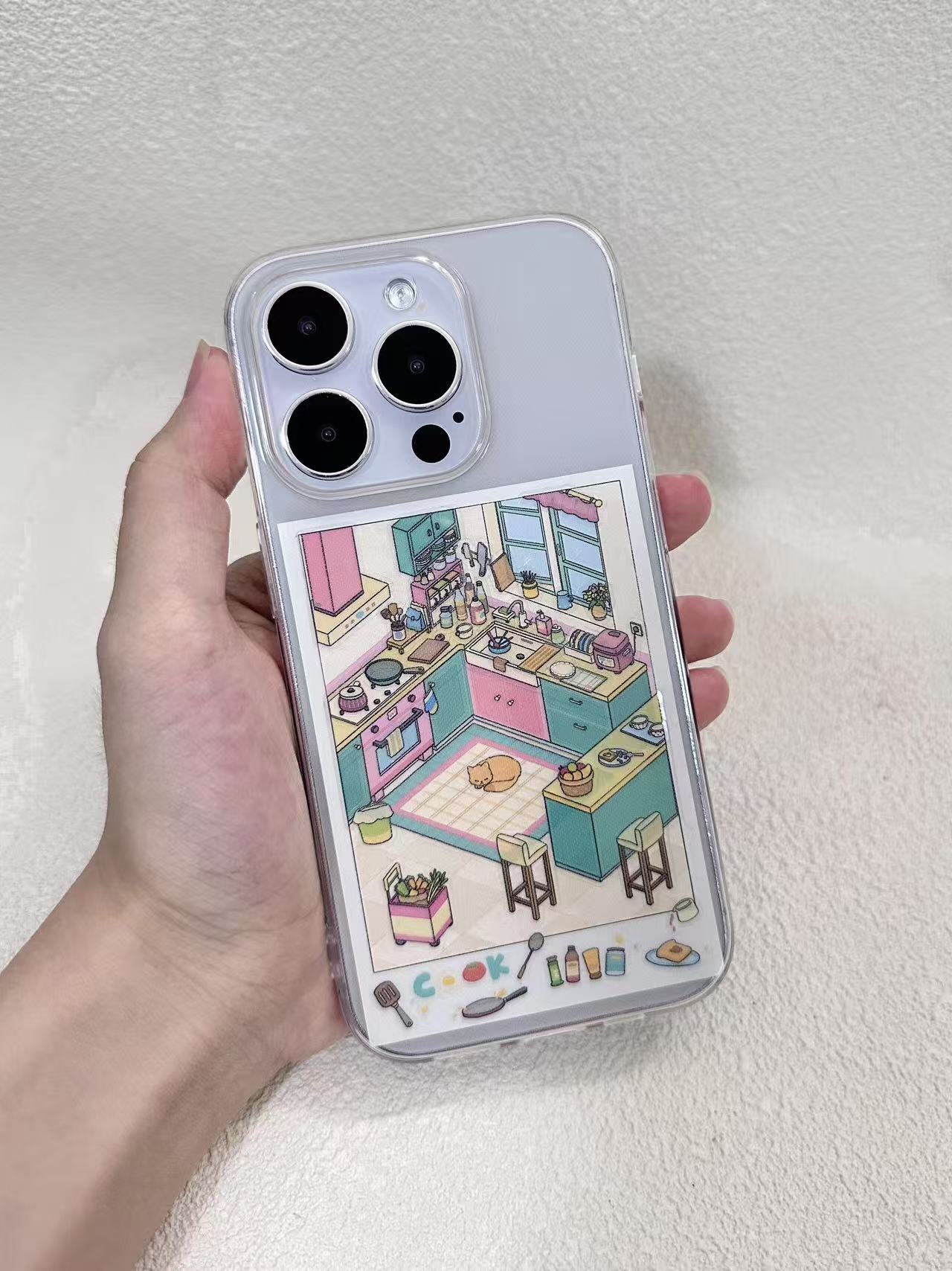 Phone case with a colorful kitchen illustration held by a hand against a light gray background