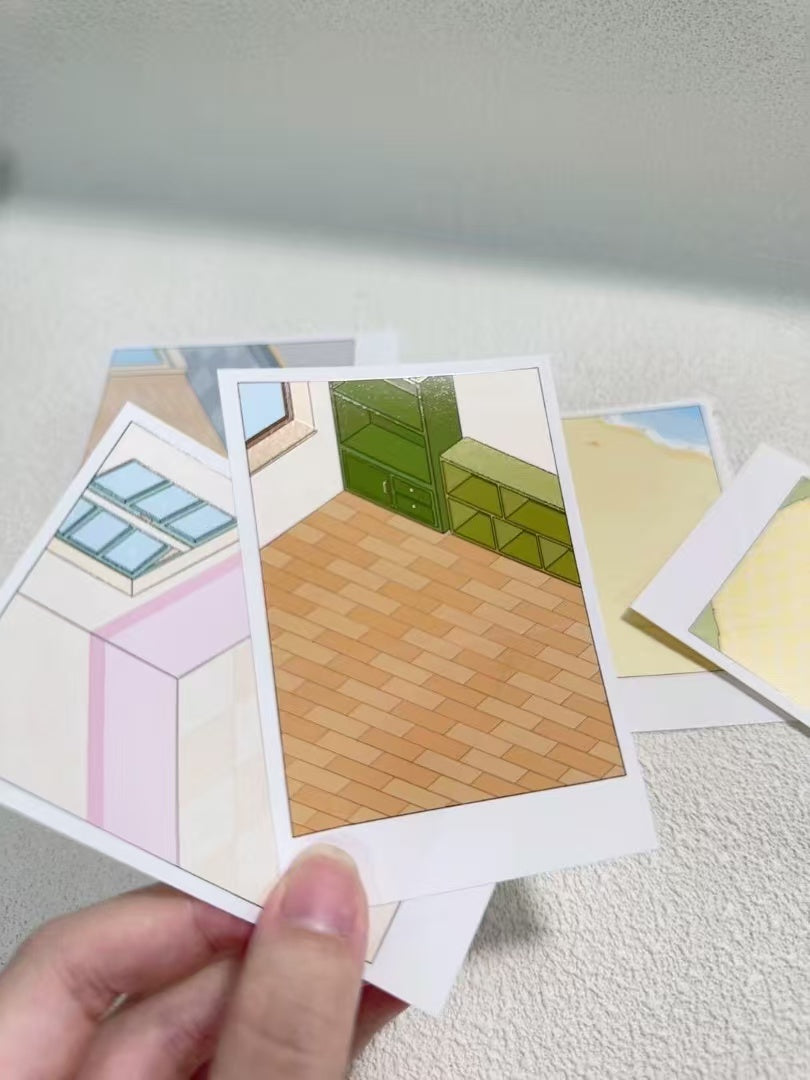 Hand holding a set of small cards with room layout illustrations on a light surface.